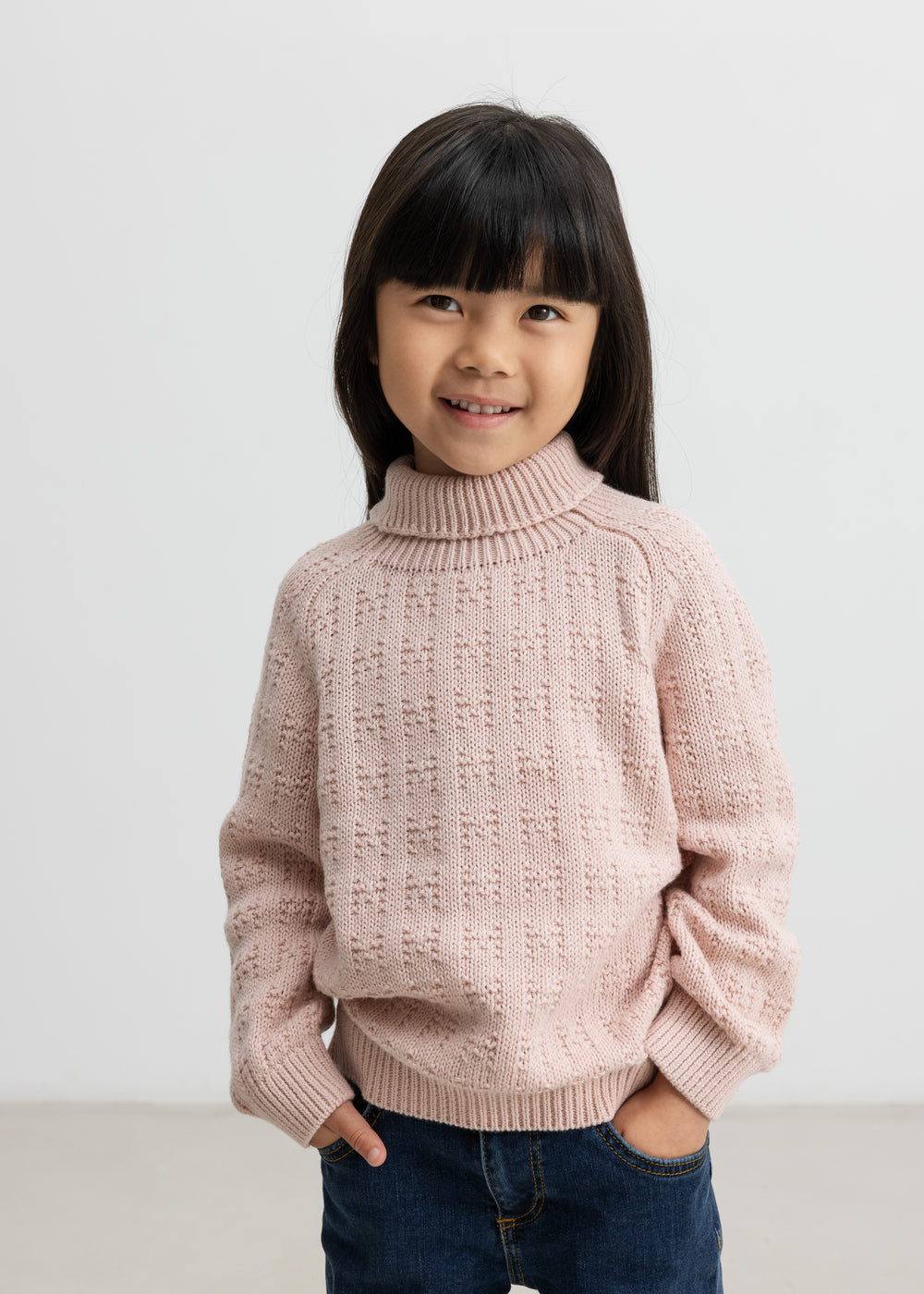 Barn iført lyserød striktrøje med rullekrave og mørkeblå jeans, smilende