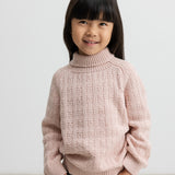 Barn iført lyserød striktrøje med rullekrave og mørkeblå jeans, smilende