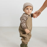 Baby iført brun M-mønstret striktrøje, termobukser og hue, holder en voksen i hånden