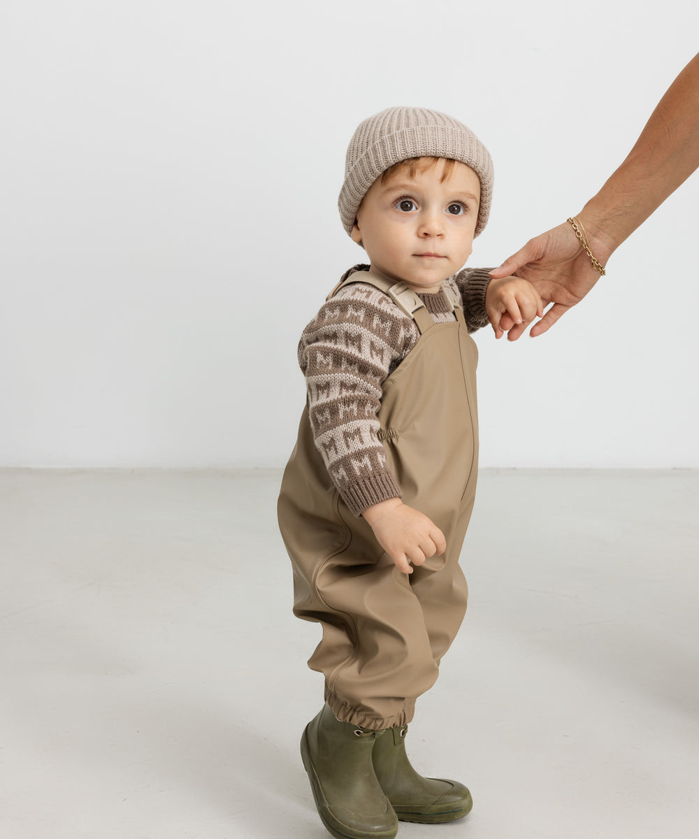 Barn iført beige strikhue og termotøj, håller en voksen i hånden