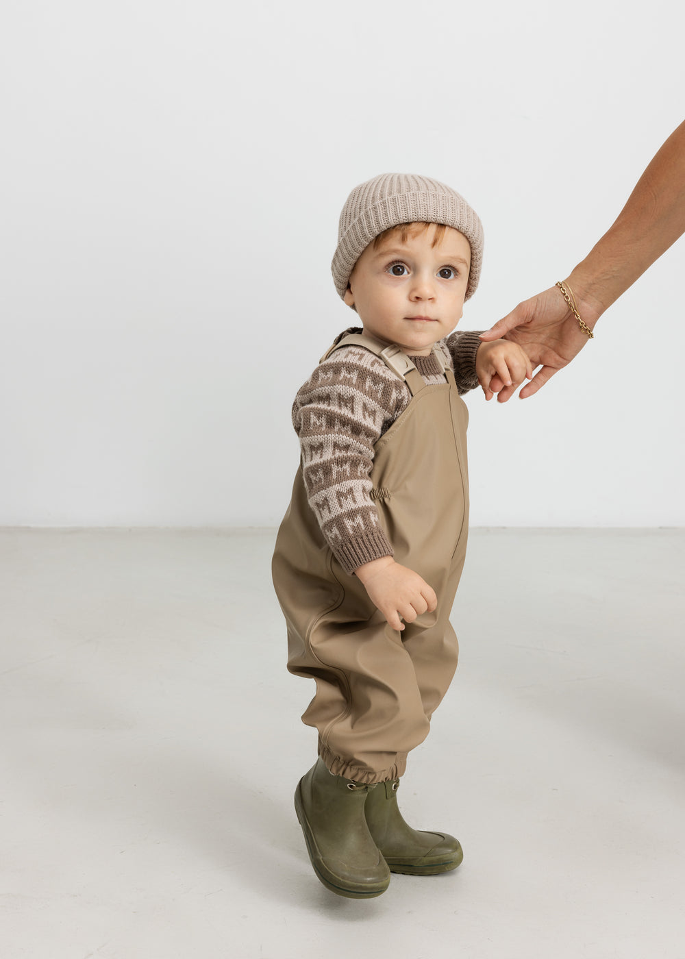 Barn iført beige strikhue og termotøj, håller en voksen i hånden