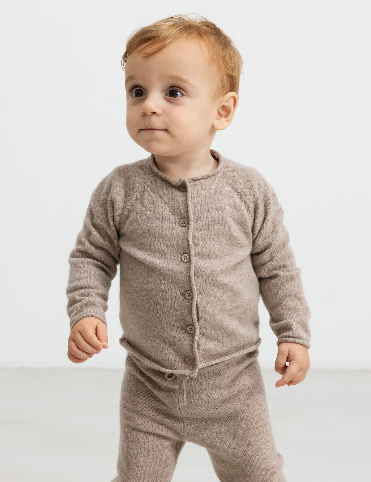 Baby i beige strikket cardigan og bukser