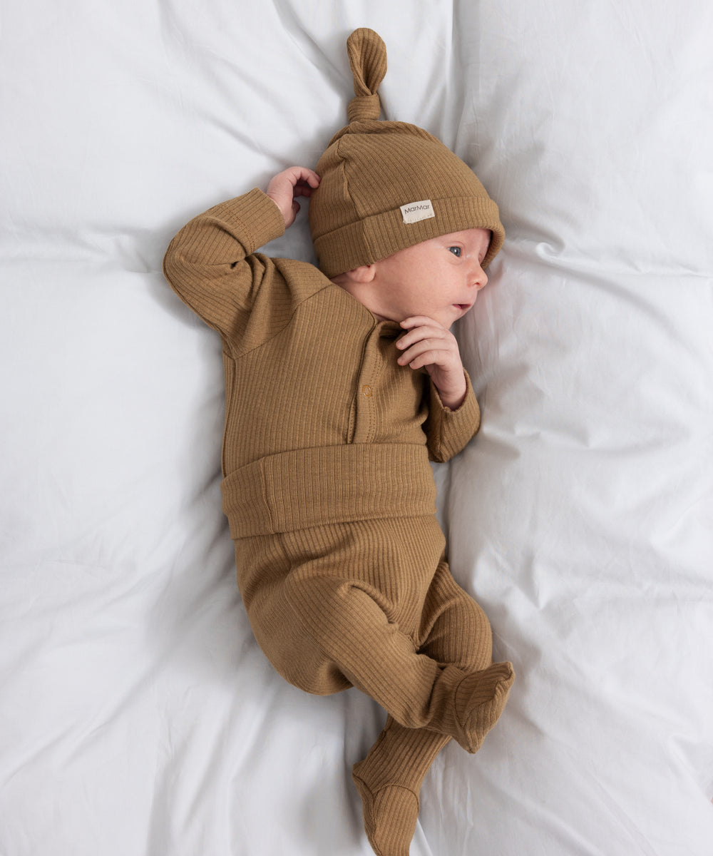 Baby iført brune ribstrikkede babybukser med nedbukket kant og futter, babybody og babyhue