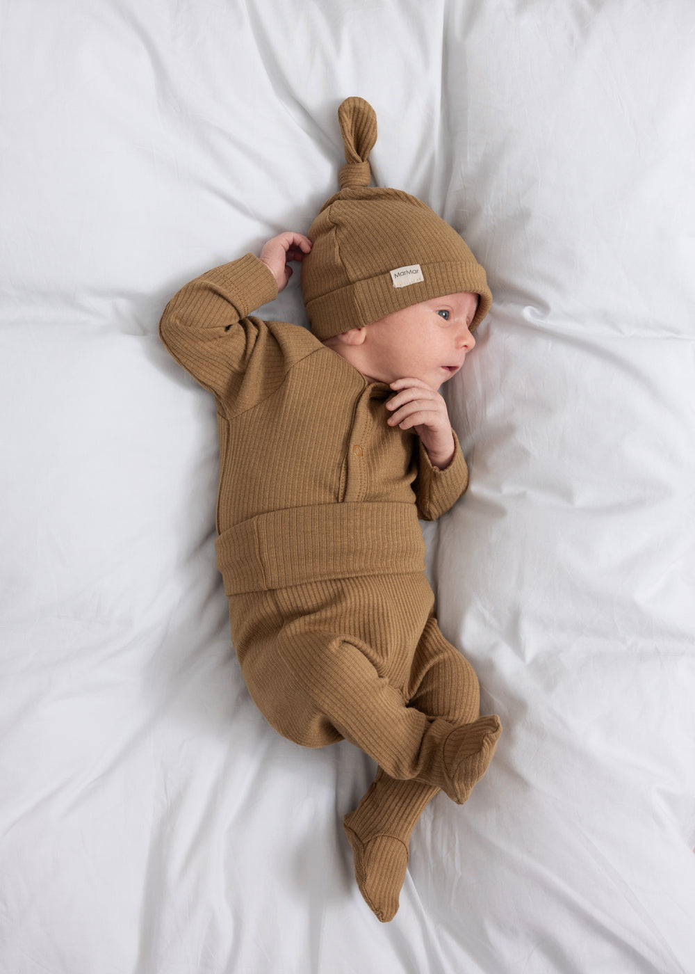 Baby iført brun ribstrikket babybody med knapper foran og babyhue