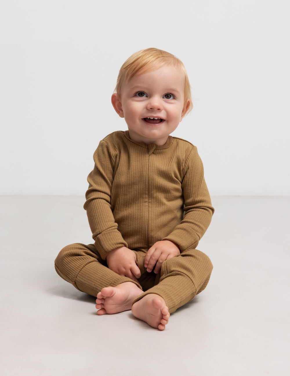 Baby iført ribbstrikket brun holdragt i blødt materiale med lange ærmer og lange ben og lynlås