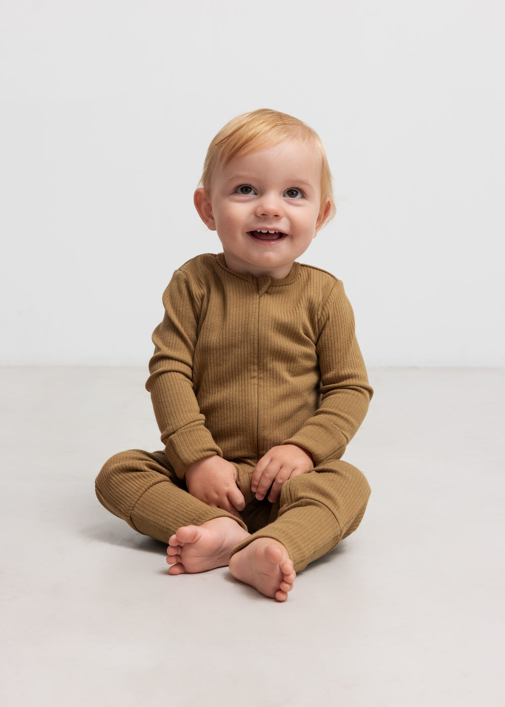 Baby iført ribbstrikket brun heldragt i blødt materiale med lange ærmer og lange ben og lynlås