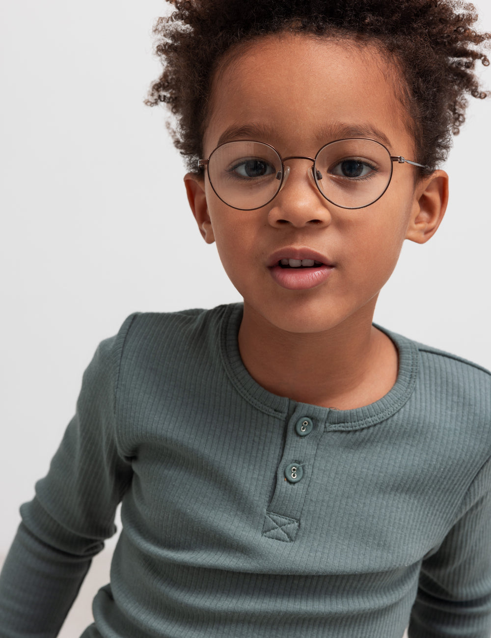 Dreng iført grøn ribbstikket t-shirt med knapper og briller.