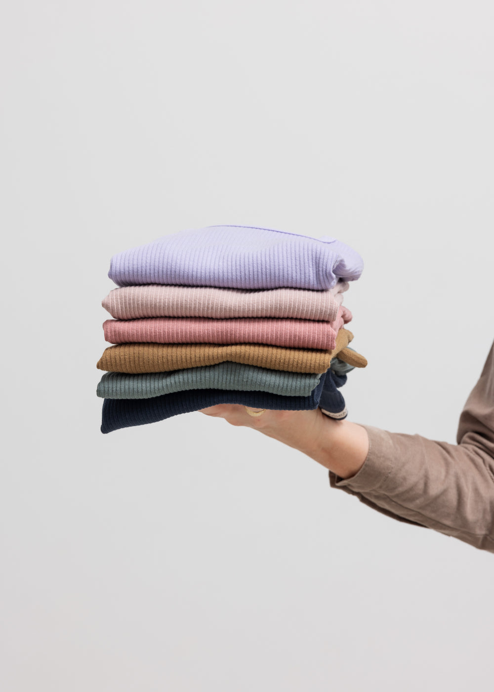 Person holder foldede børne t-shirts i forskellige farver