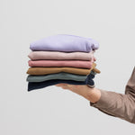 Person holder foldede børnetrøjer i forskellige farver, inkl. navyblå ribstrikket t-shirt