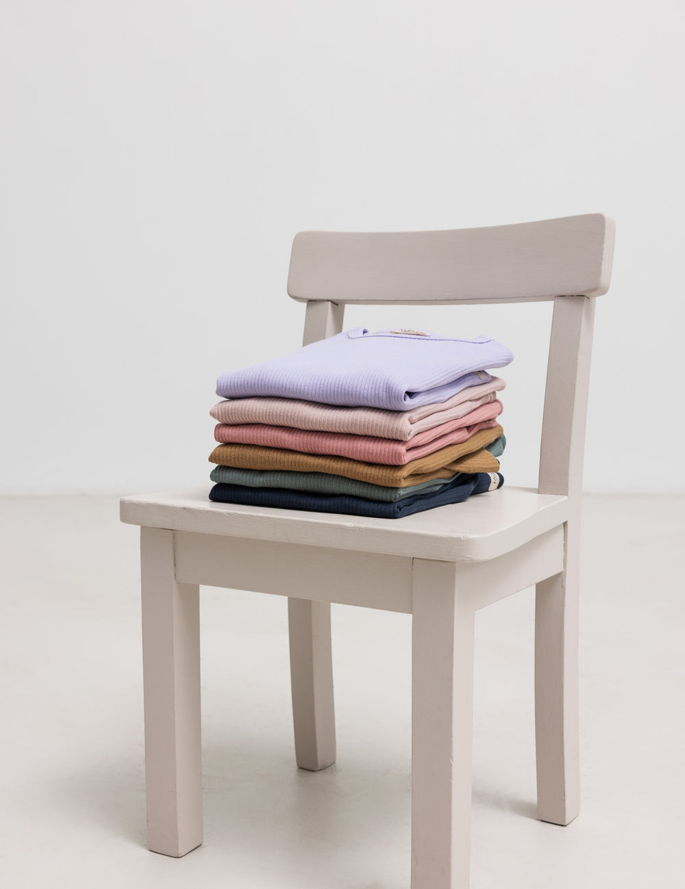 Stak af børne t-shirts i flere farver placeret på stol