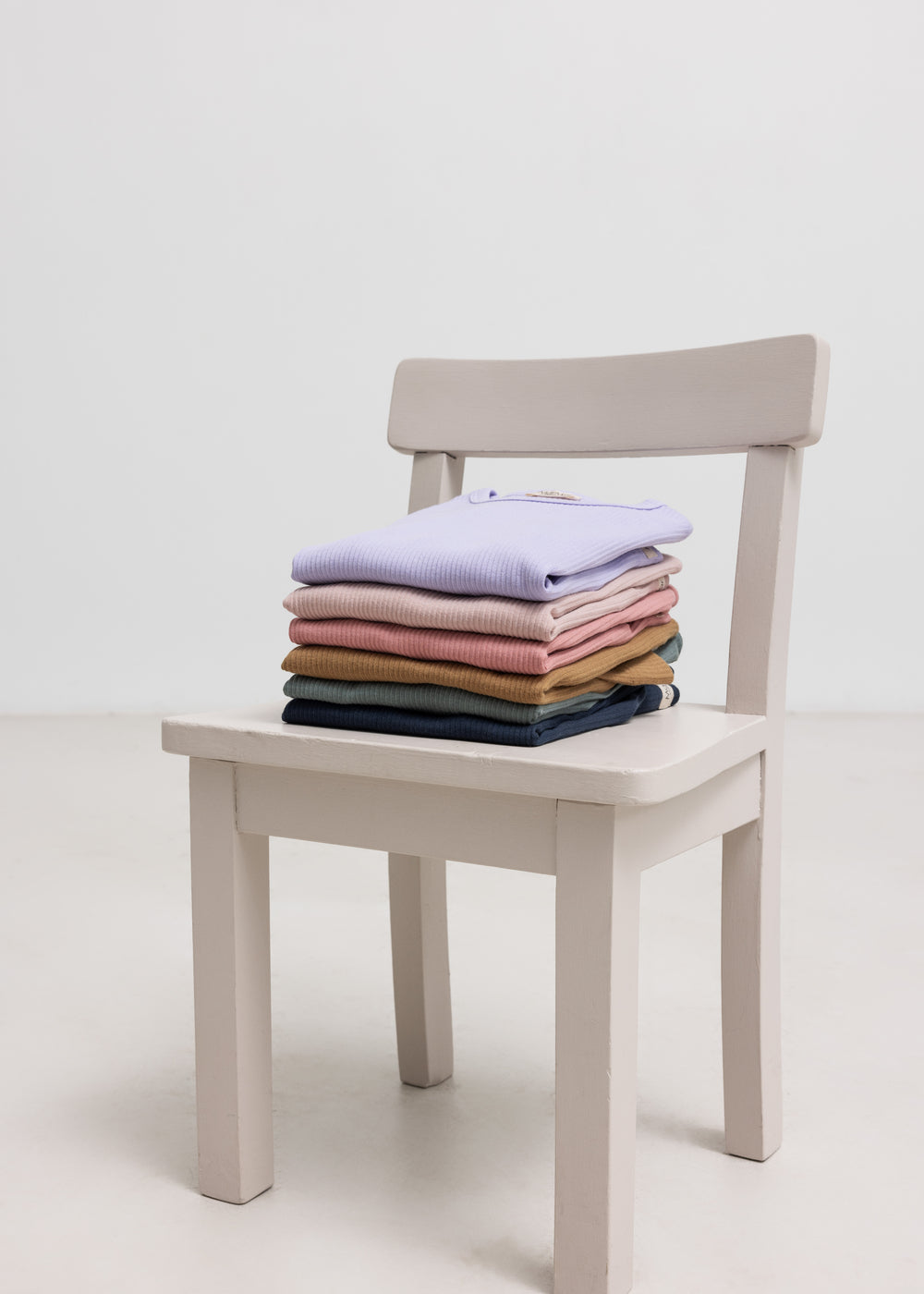 Foldede børnetrøjer på en stol, med navyblå ribstrikket t-shirt