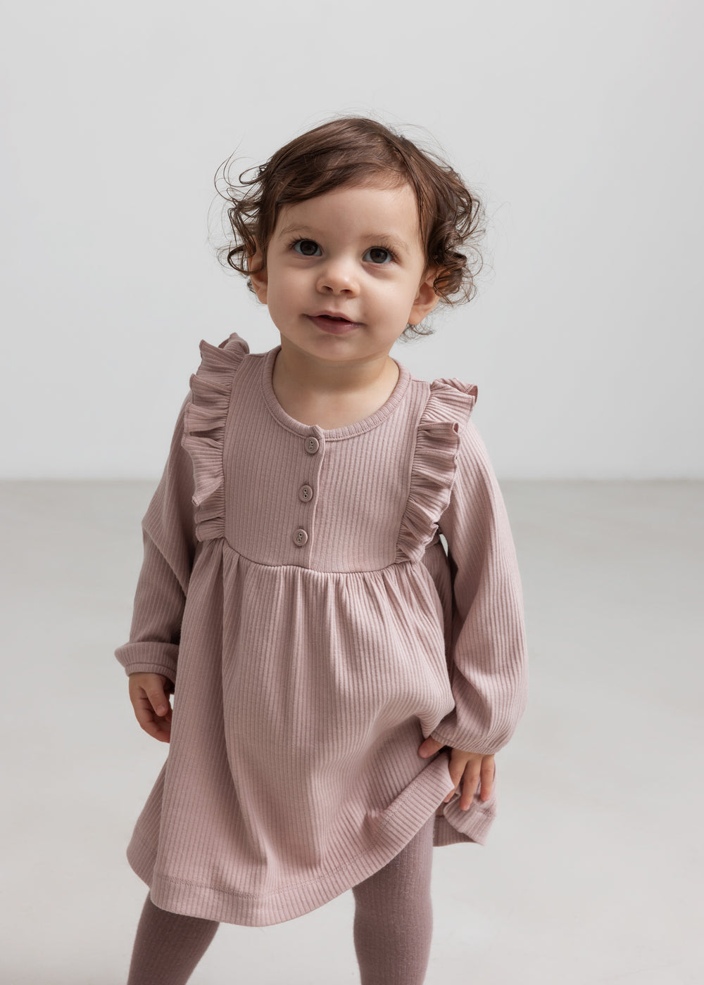 Børn iført lyserød ribstrikket kjole med flæsedetaljer og lange ærmer