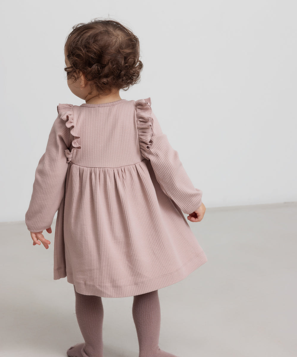 Børn iført lyserød ribstrikket kjole med flæsedetaljer og lange ærmer