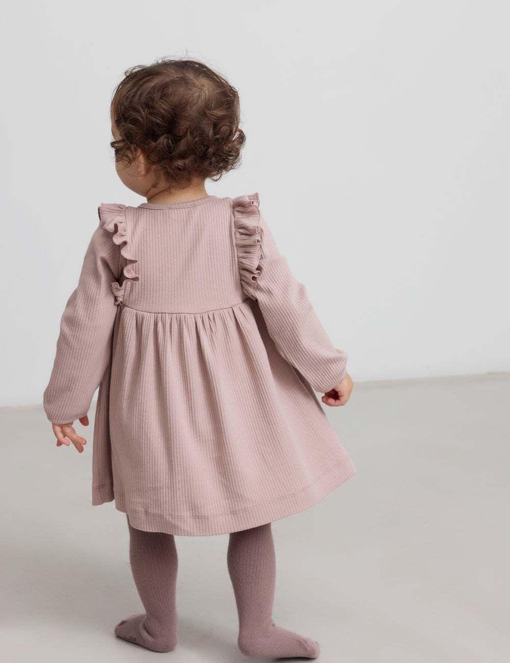 Børn iført lyserød ribstrikket kjole med flæsedetaljer og lange ærmer