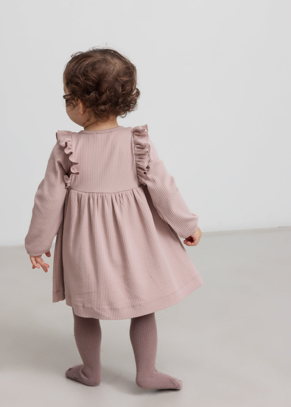 Børn iført lyserød ribstrikket kjole med flæsedetaljer og lange ærmer