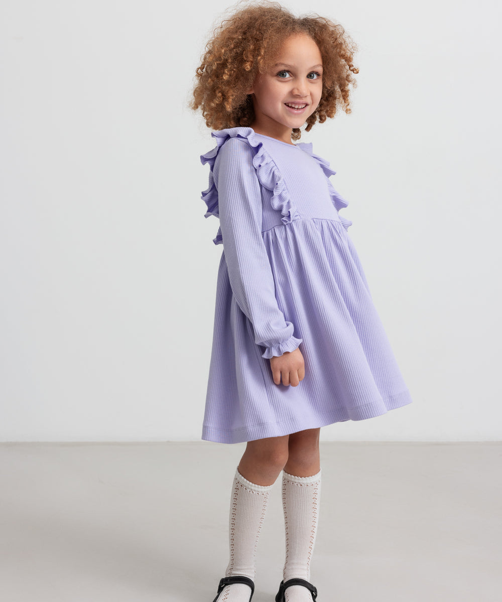 Pige i langærmet lilla ribstrikket kjole med flæser