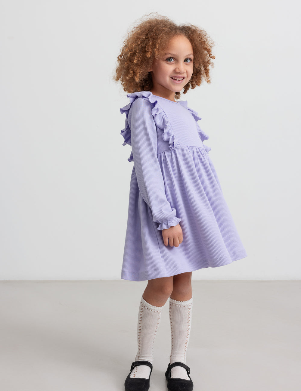 Pige i langærmet lilla ribstrikket kjole med flæser