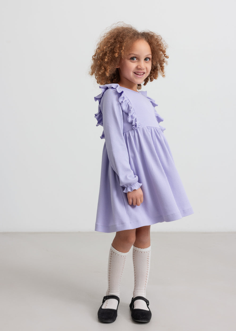 Pige i langærmet lilla ribstrikket kjole med flæser