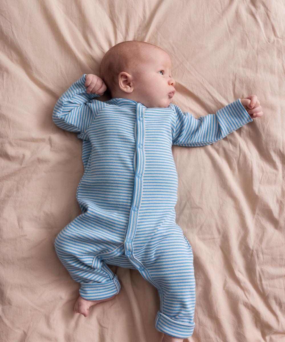 Baby iført blå og hvid stribet heldragt ligger på et beige tæppe