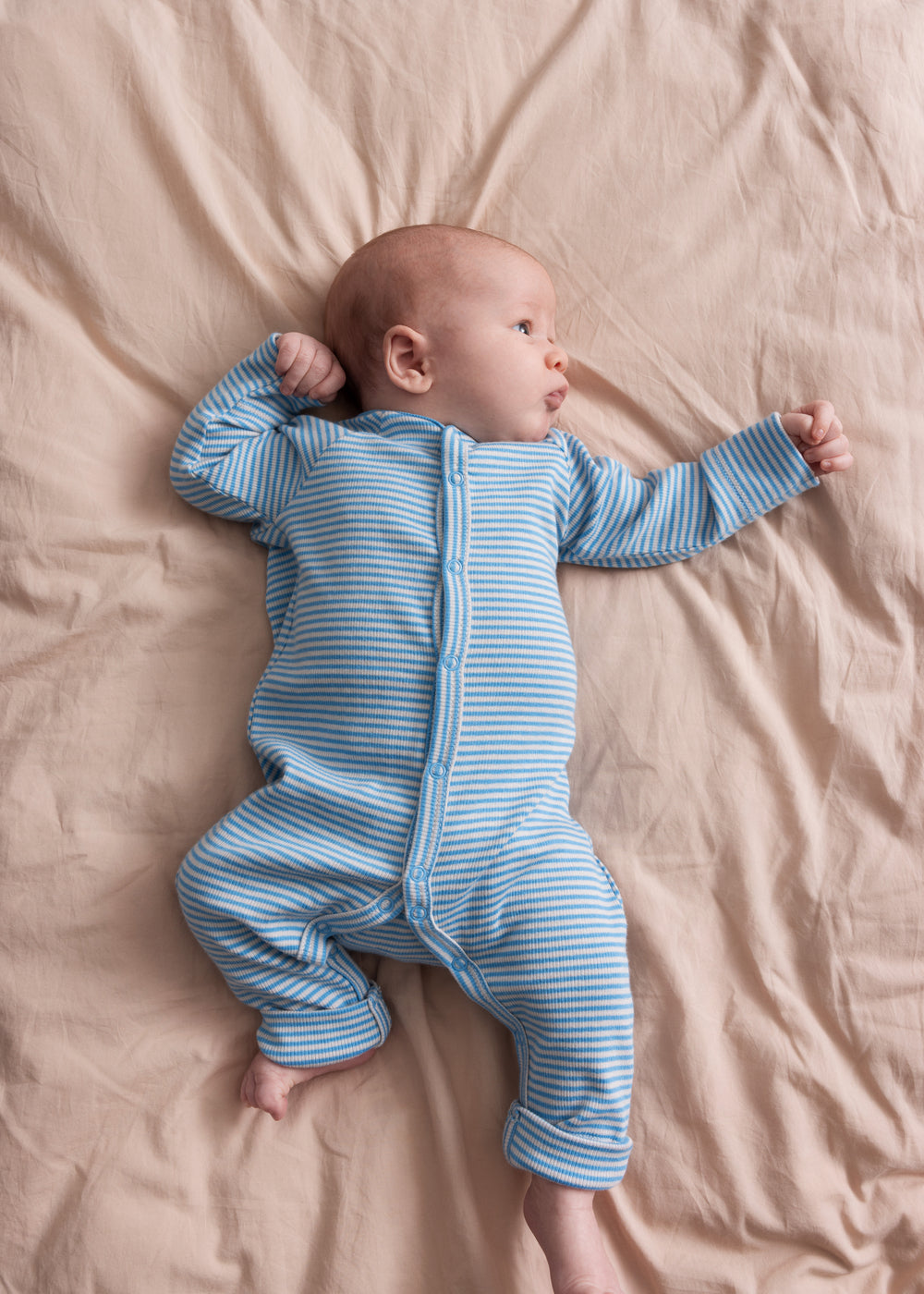 Baby iført blå og hvid stribet heldragt ligger på et beige tæppe