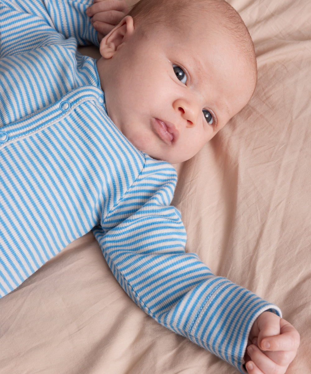 Baby iført blå- og hvidstribet body med lange ærmer, liggende på beige tæppe