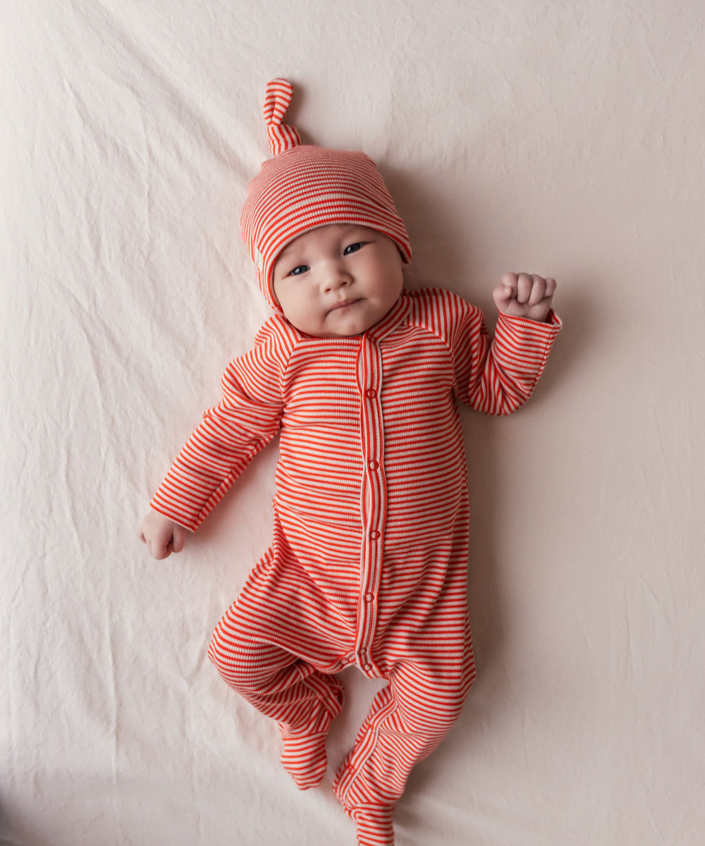 Baby iført rød heldragt og hue ligger på et tæppe