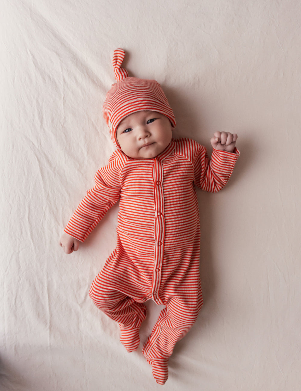 Baby wearing a red jumpsuit and hat lies on a blanket