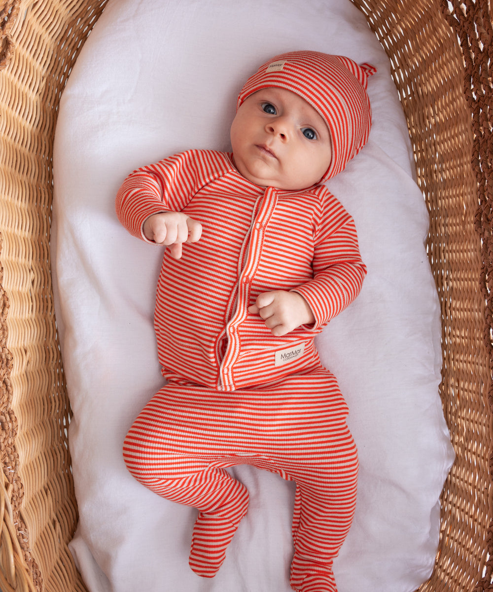 Baby iført rød og hvid stribet hue og heldragt liggende på ryggen