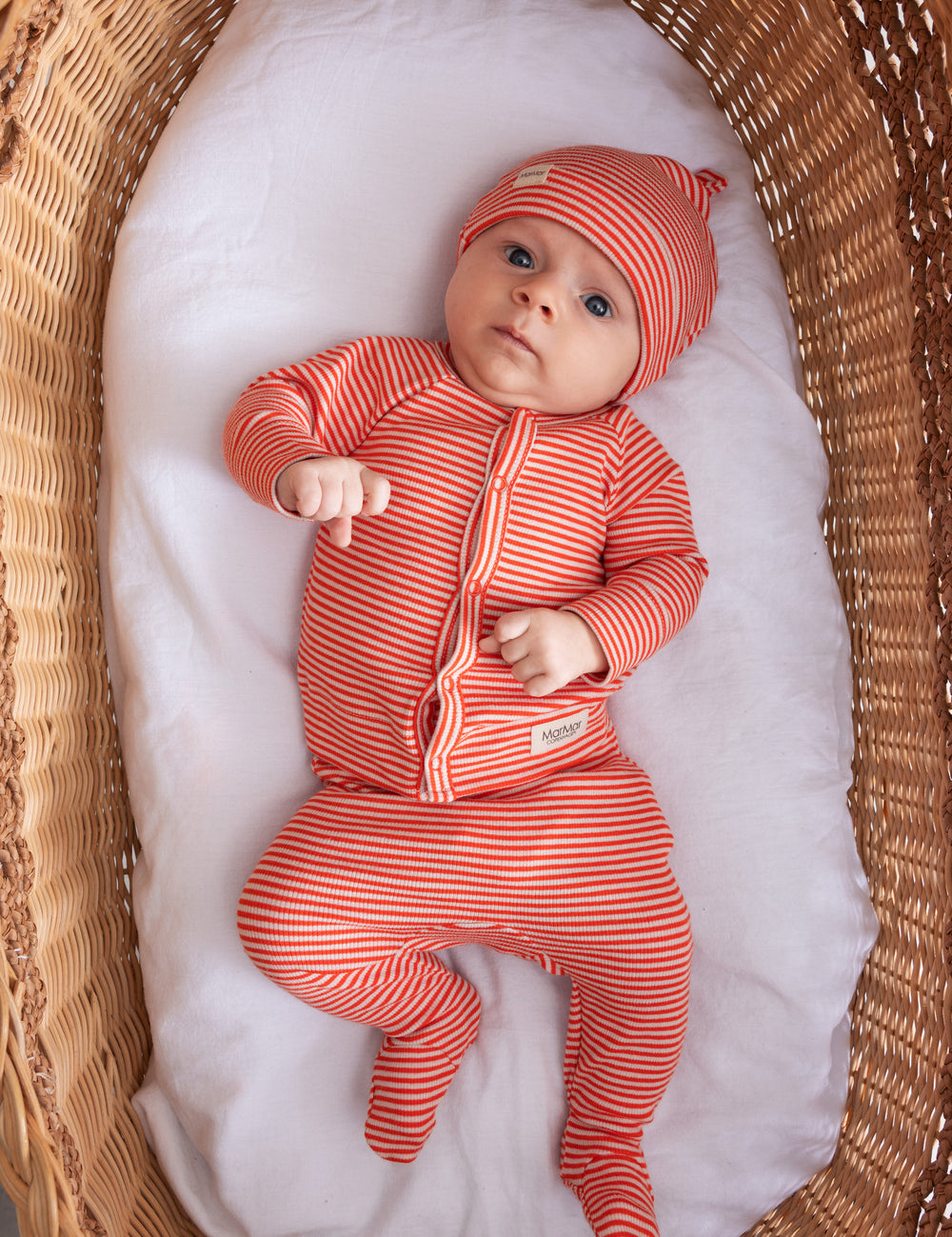 Baby wearing red and white striped hat and jumpsuit lying on back
