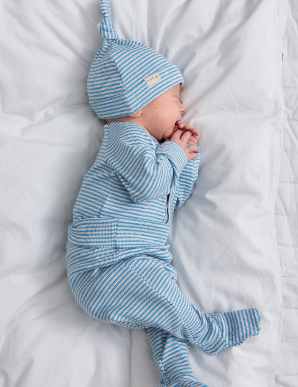 Baby wearing blue and white striped hat and jumpsuit lying on back