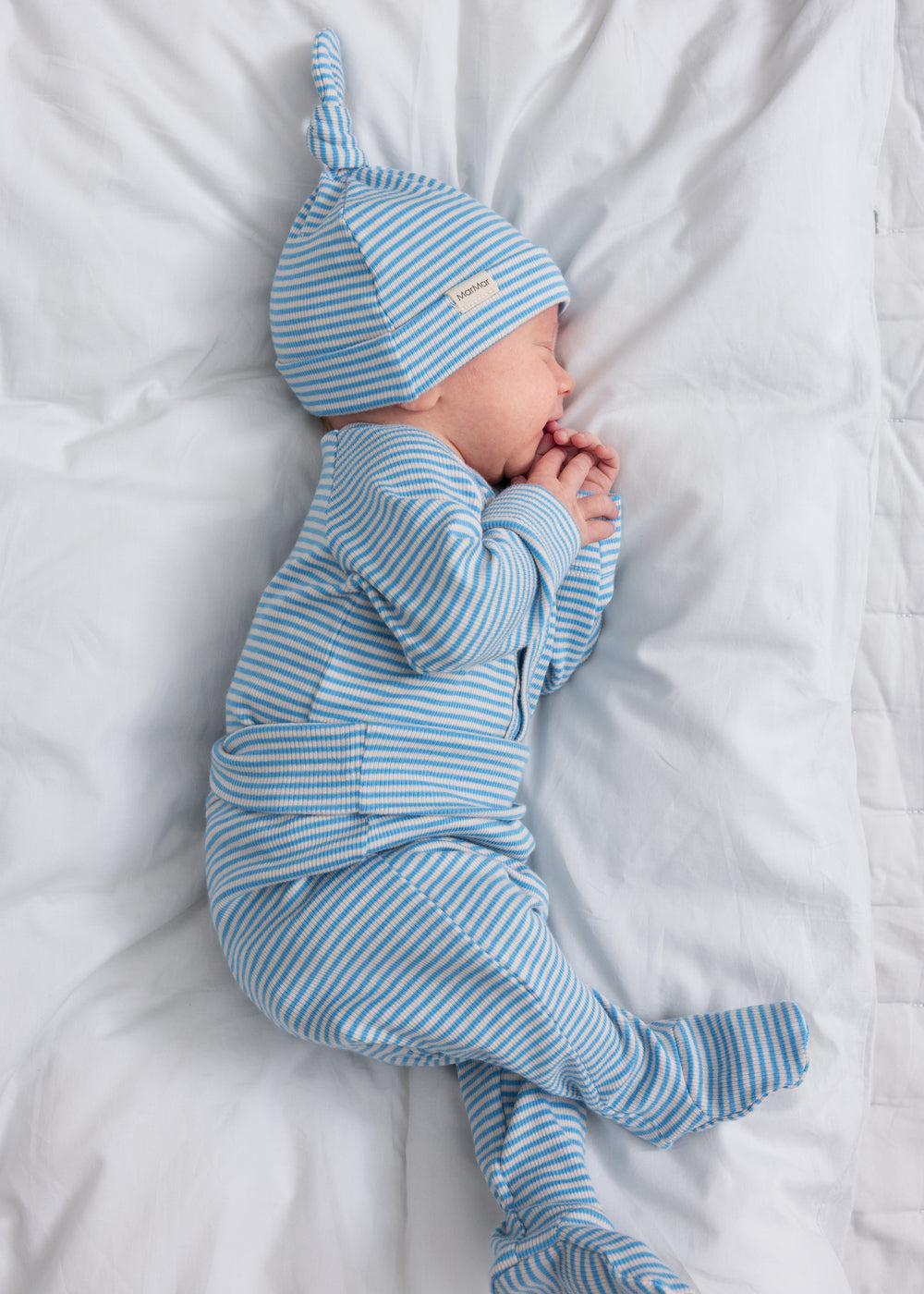 Baby iført blå og hvid stribede bukser og matchende hue sover