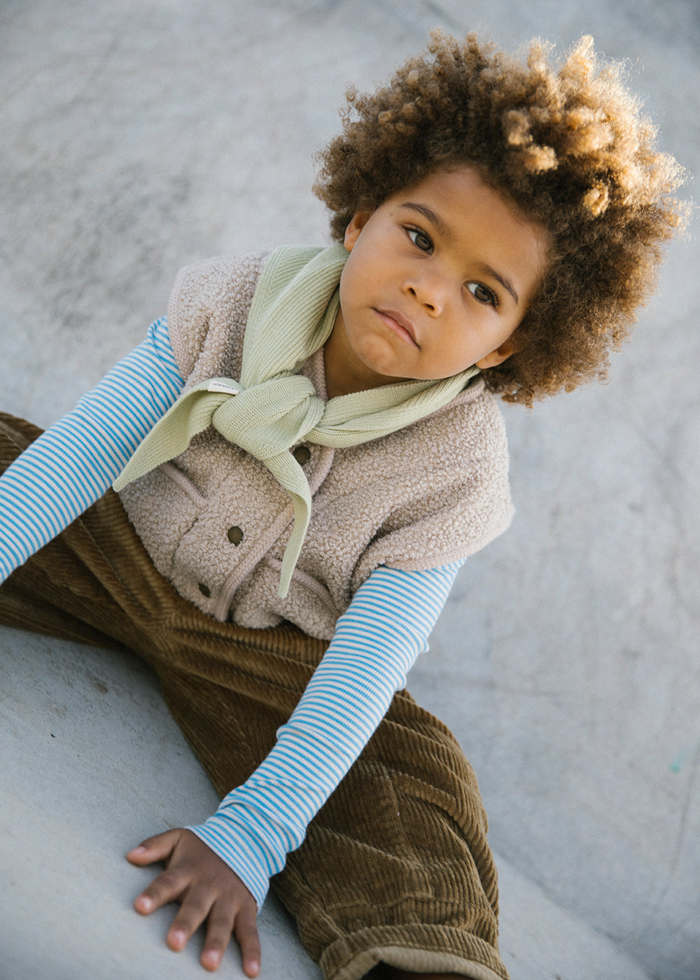Dreng iført blå og hvid stribet bluse under beige strikvest med tørklæde