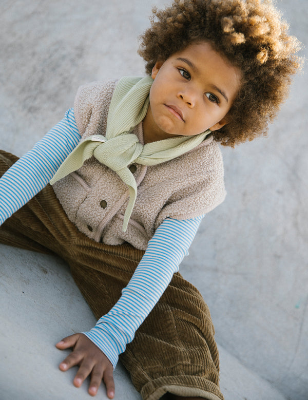 Barn iført stribet bluse, fleecevest og fløjsbukser