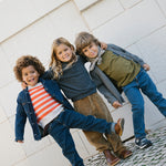 Tre børn iført strikkede cardigans og jeans leger udendørs