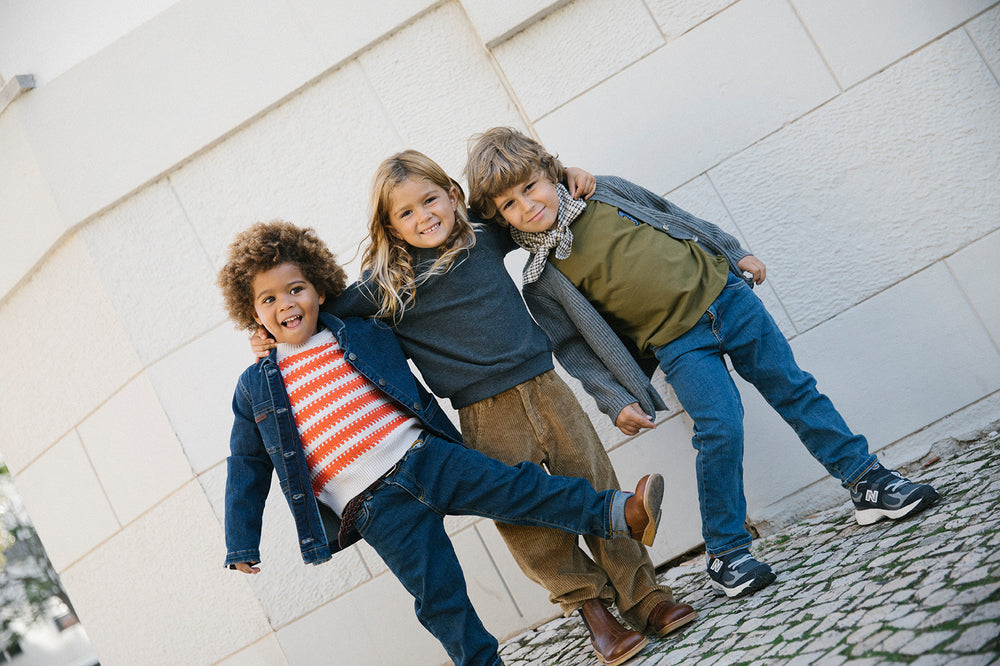 Tre børn iført strikkede cardigans og jeans leger udendørs