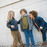 Tre børn i fløjlsbukser og cardigans leger foran mur