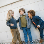 Tre børn iført strikkede cardigans og jeans leger udendørs