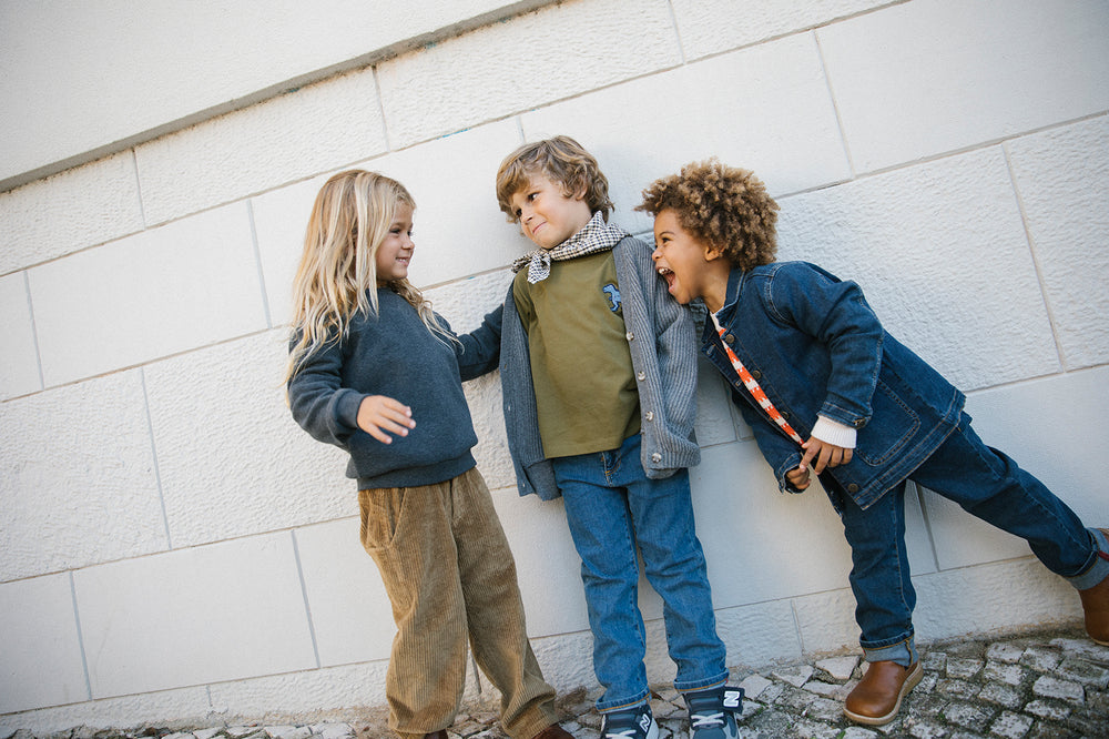 Tre børn iført strikkede cardigans og jeans leger udendørs