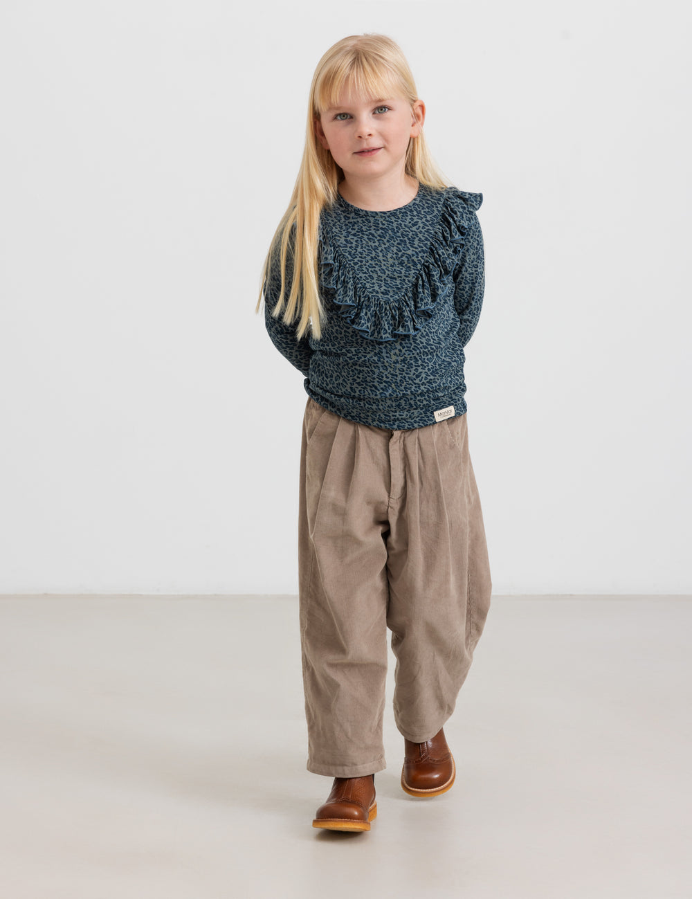 Pige iført beige babyfløjlssbukser og mørkeblå bluse