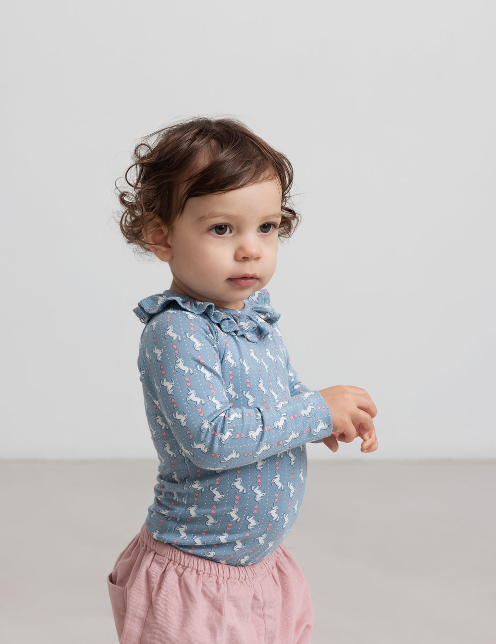 Baby wearing blue bodysuit with unicorn pattern and ruffle collar