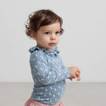 Baby iført blå body med enhjørningemønster og flæsekrave