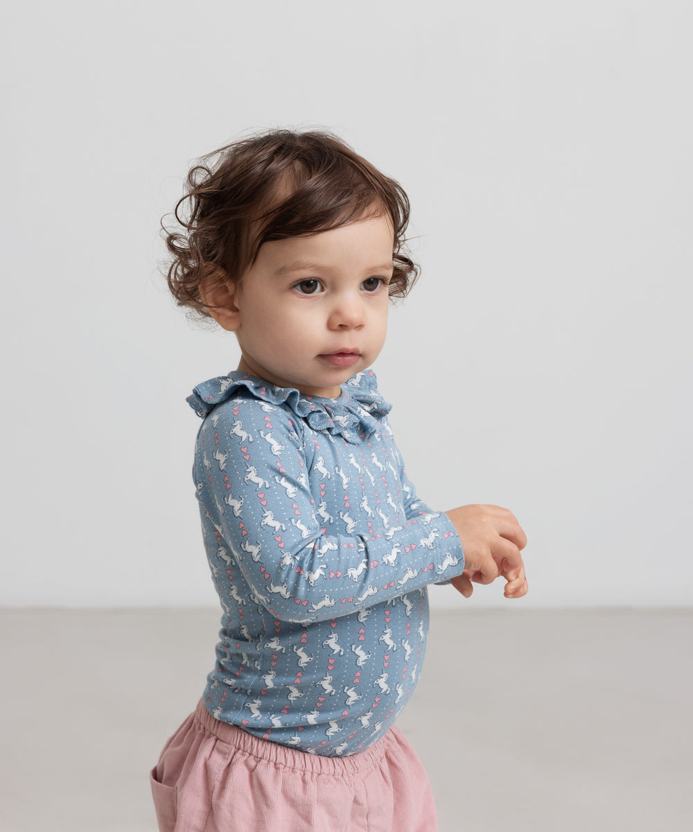 Baby iført lyserøde bukser og blå bluse med unicornprint