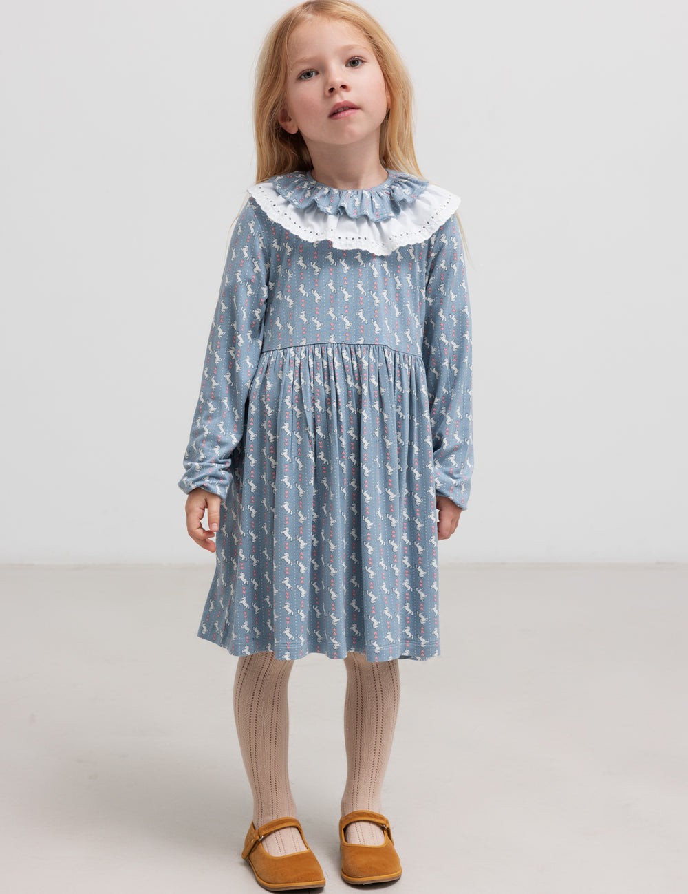Pige iført blå kjole med enhjørningemønster og flæsekrave