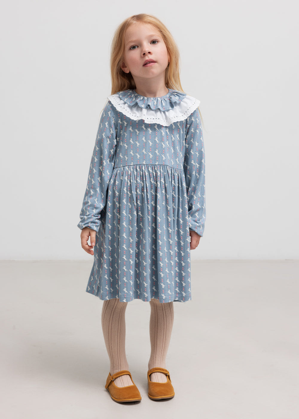 Pige iført blå kjole med enhjørningemønster og flæsekrave