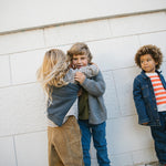 Tre børn iført strikkede cardigans og jeans leger udendørs