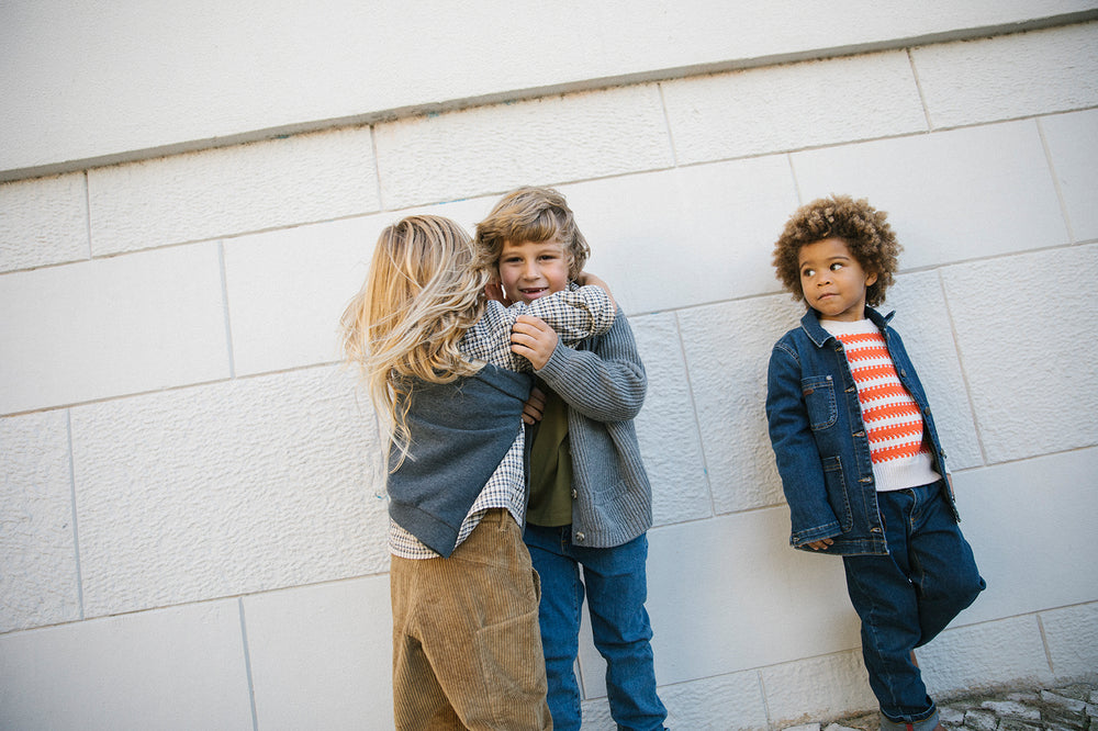 Tre børn iført strikkede cardigans og jeans leger udendørs