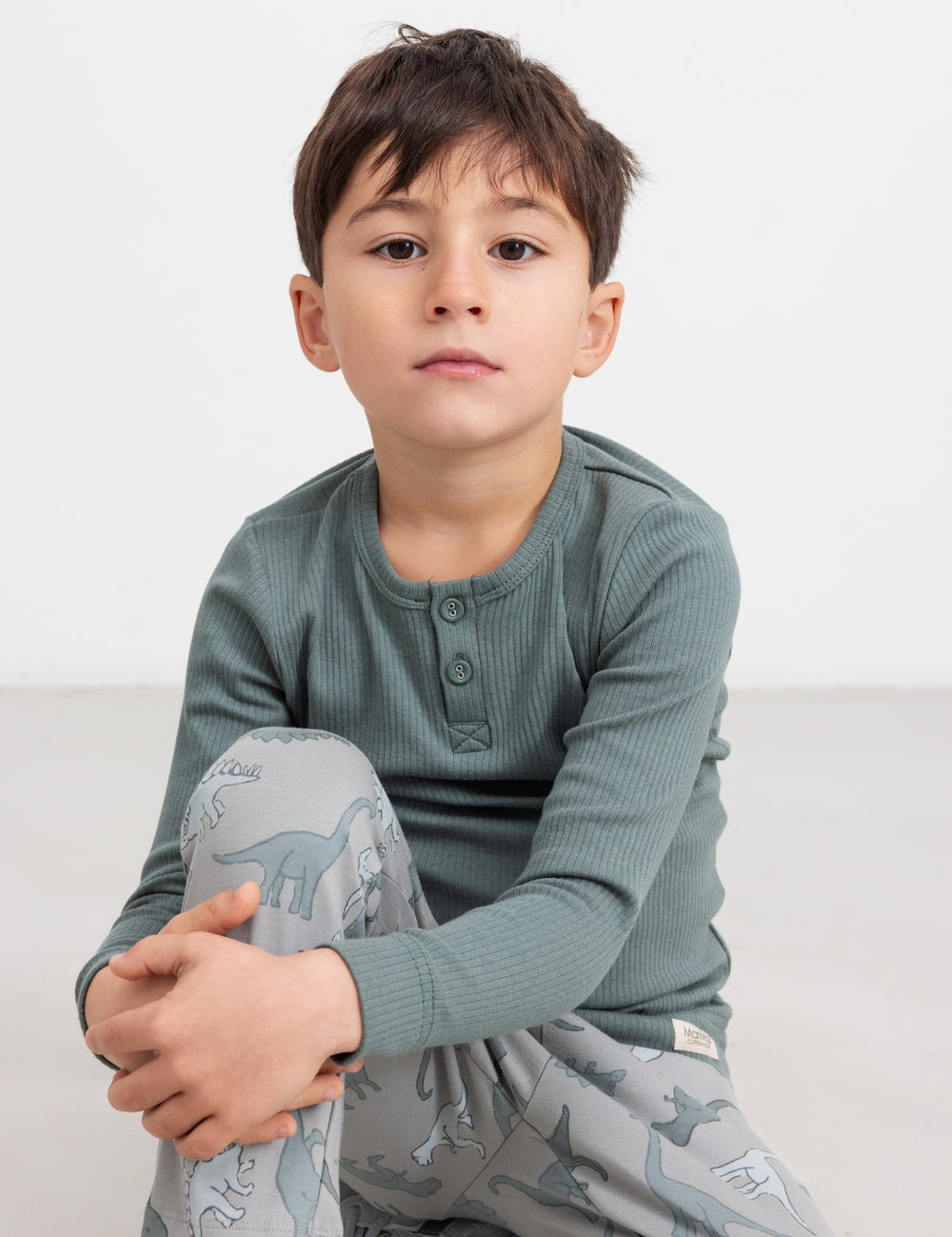 Dreng iført grøn ribbluse med knapper sidder på gulvet.