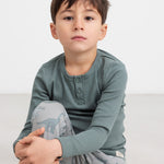 Dreng iført grøn ribbluse med knapper sidder på gulvet