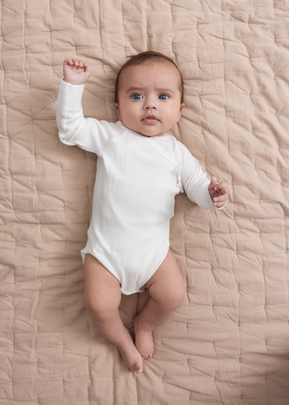 Baby iført hvid pointelle slå-om body liggende på quiltet tæppe