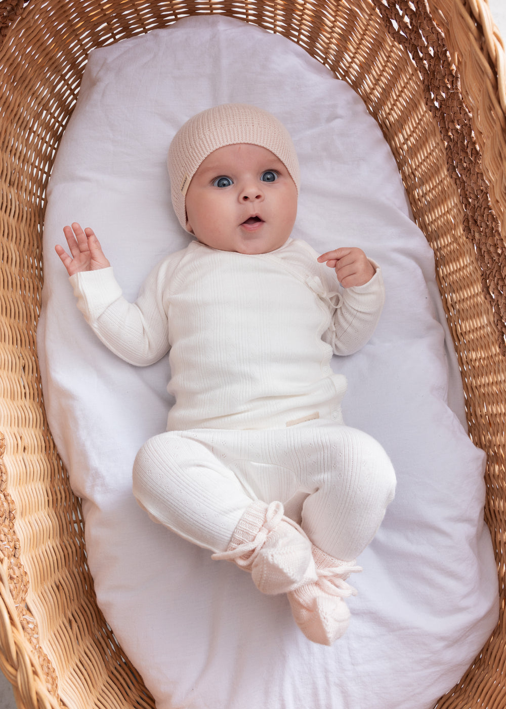 Baby iført hvid pointelle slå-om bluse og bukser liggende i kurv